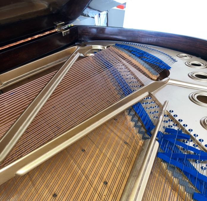 Inside a grand piano showing the strings, dampers and gold cast-iron frame